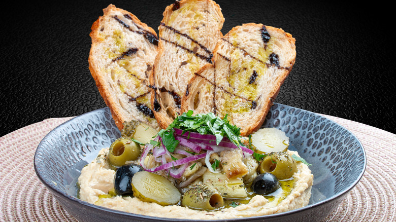 Bowl of hummus with crostini, pickles, onions, and olives