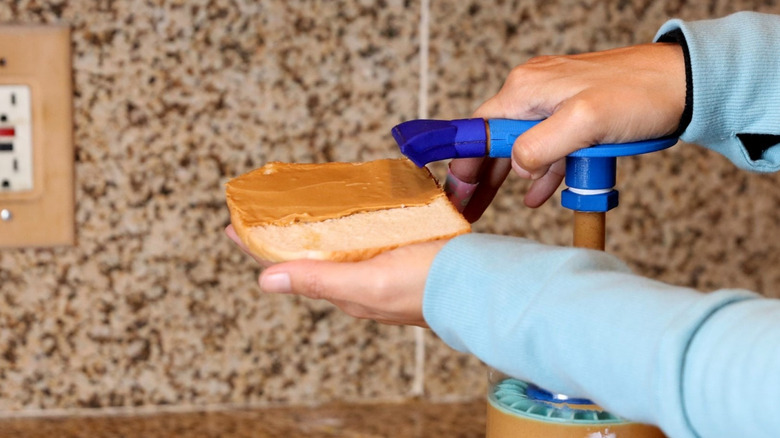 Closeup of hands using a Peanut Butter Pump to pump peanut butter onto a slice of bread