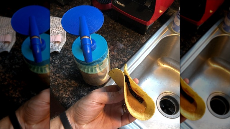 A peanut butter pump sits next to a sink, as someone holds a peanut butter and jelly taco