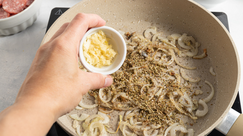 adding garlic and oregano to pan of onions