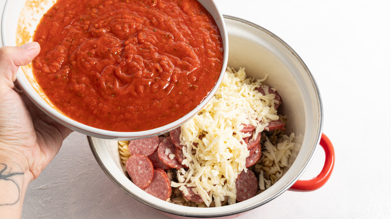 assembling pepperoni cheese and tomato sauce pasta dish