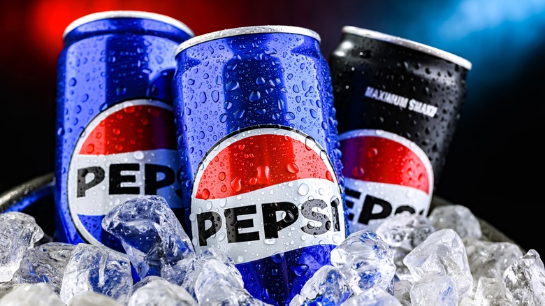 Three cans of Pepsi, two blue and one black, sit in a bed of cubed ice