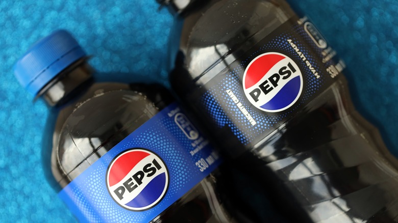 A close-up shot of two Pepsi bottles with different colored labels, one light blue and one black