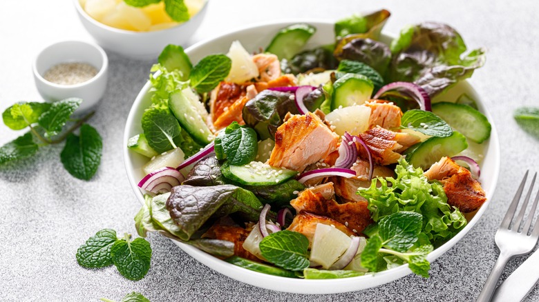 White bowl of green salad with salmon and red onion