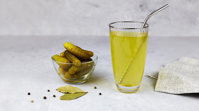 A glass of pickle brine beside bowl of pickles