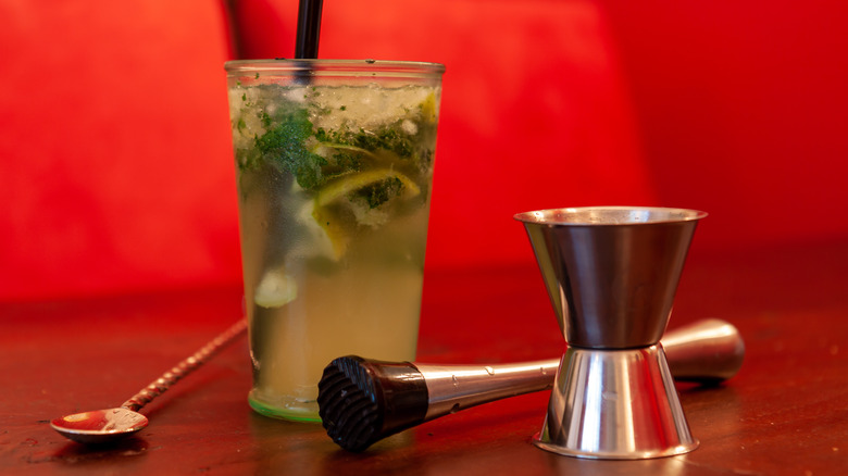 Glass of mojito cocktail with a muddler, jigger, and bar spoon