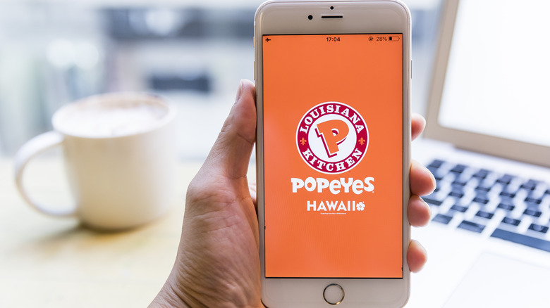 Person holding phone with Popeyes app