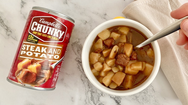 Campbell's Chunky Steak and Potato soup in a bowl with can and spoon on counter