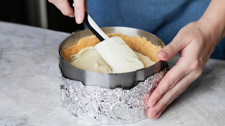 Cheesecake being assembled in springform pan wrapped in foil