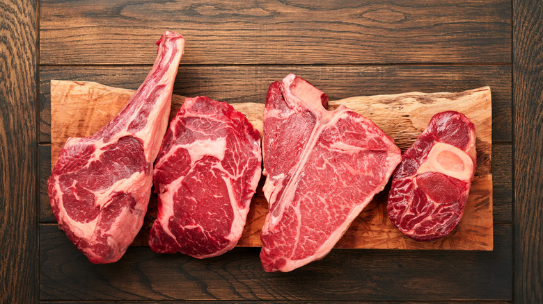 Four cuts of raw meat on a plank on a wooden table