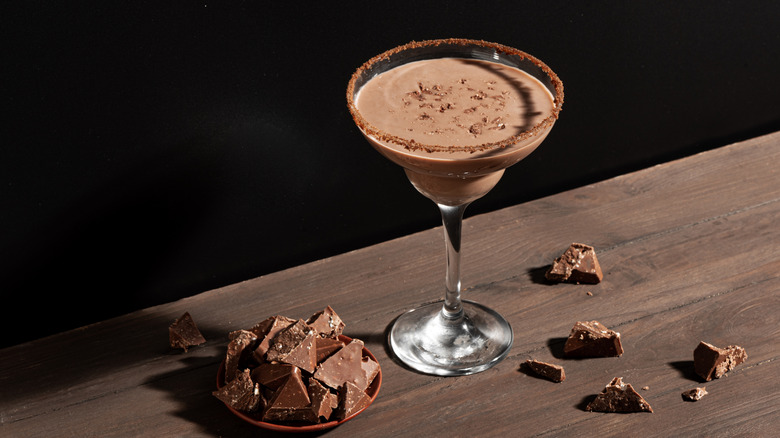 A chocolate martini surrounded by chocolate pieces sitting near the edge of a table