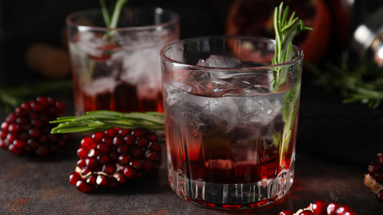 Pomegranate cocktails in rocks glasses with rosemary and pomegranate pieces surrounding them