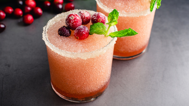 Two frozen cranberry margaritas with sugar rims and a pile of cranberries