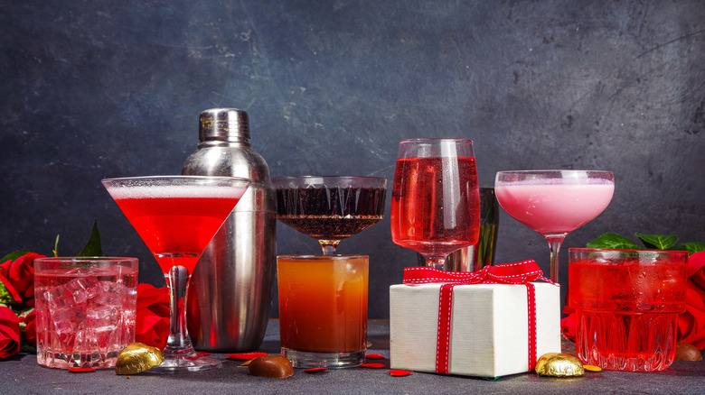 A row of pink and red cocktails in various glasses with Valentine's Day theme decor around them