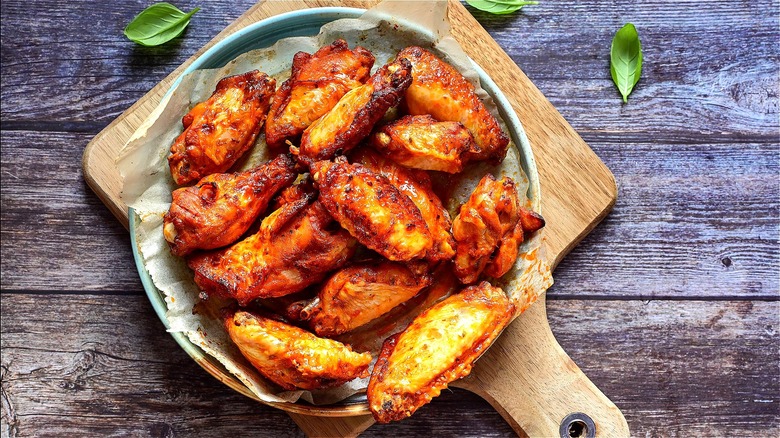 Roasted chicken wings on a parchment lined plate on top of a wooden cutting board