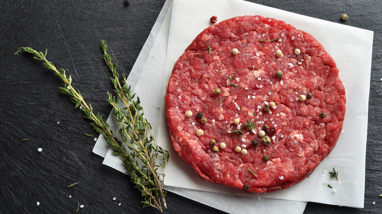 raw burger patty seasoned with salt, pepper, and herbs