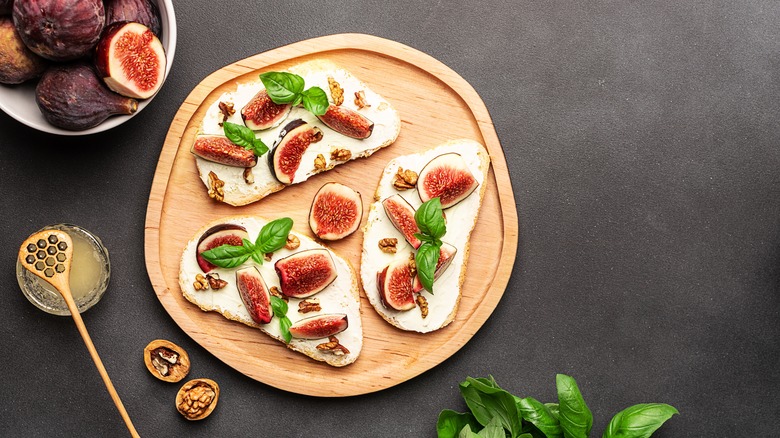 Three slices of toast topped with cream cheese or mascarpone, figs, basil, walnuts, and honey sit on a plate