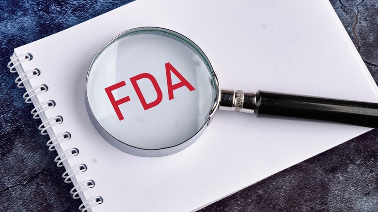 A magnifying glass lays overtop of the word 'FDA' on a white page of a notebook