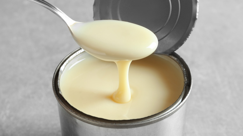 Open can of sweetened condensed milk with a spoon