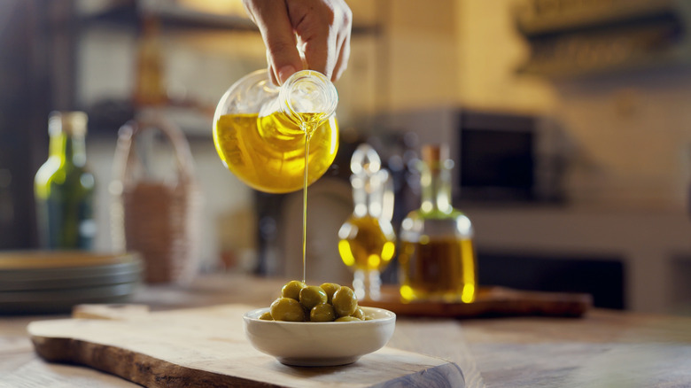 Hand pouring olive oil over a dish of green olives