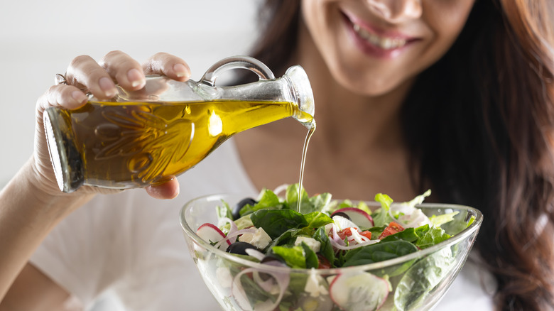 a person pouring olive oil onto salad