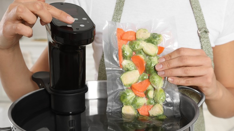 Person submerging a bag of vegetables into a sous vide bath