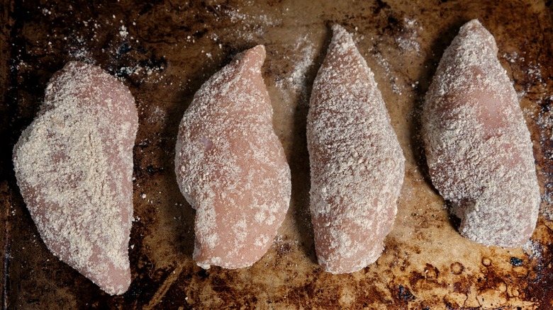 Raw chicken lightly coated with flour on a metal baking sheet