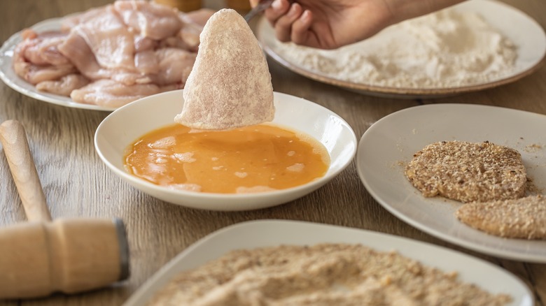 Hand dipping piece of chicken in egg for breading