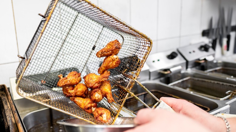 Hands dumping fried chicken from deep fryer basket