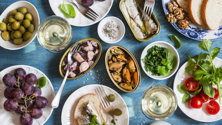 Open tins of seafood and snacks with white wine glasses