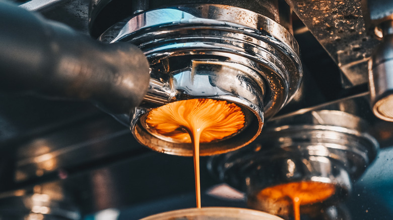 Espresso shots being poured out of espresso machine into a clear cup