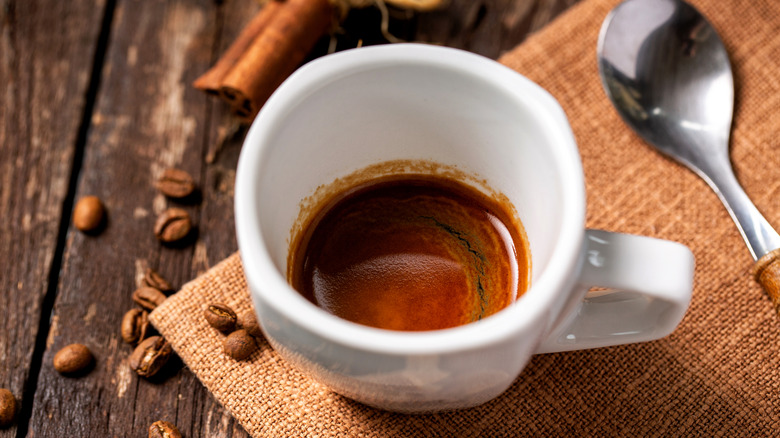 Ristretto espresso shot in white cup on a wooden background with coffee beans spread around, and spoon to the right