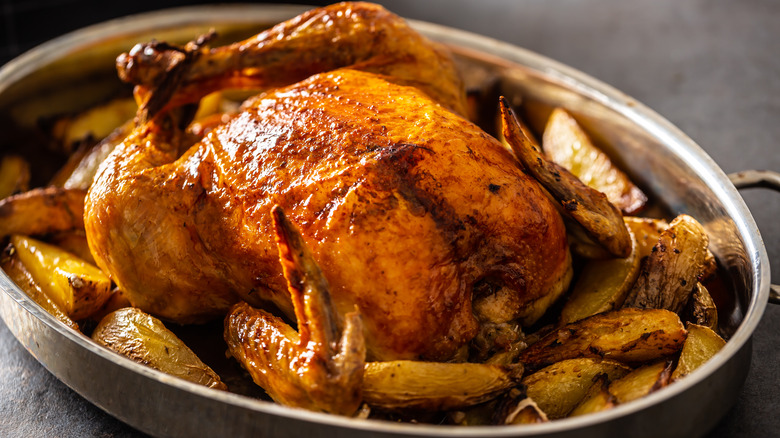 Whole roast chicken in pan with potatoes