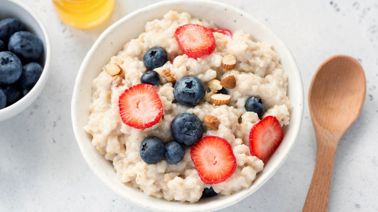 A white bowl of oatmeal topped with berries and chopped almonds next to a wooden spoon