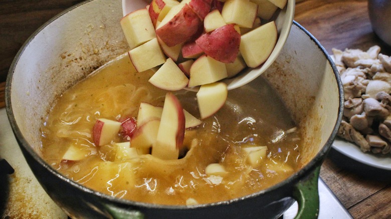 adding potatoes to soup pot