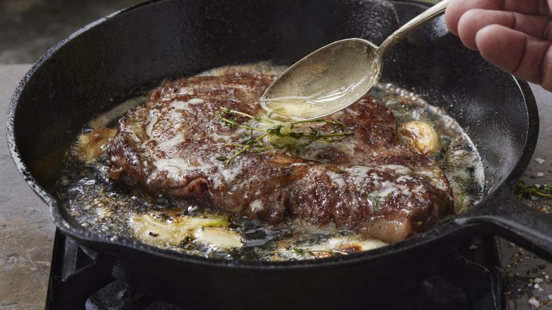 Steak being basted with garlic butter in hot pan