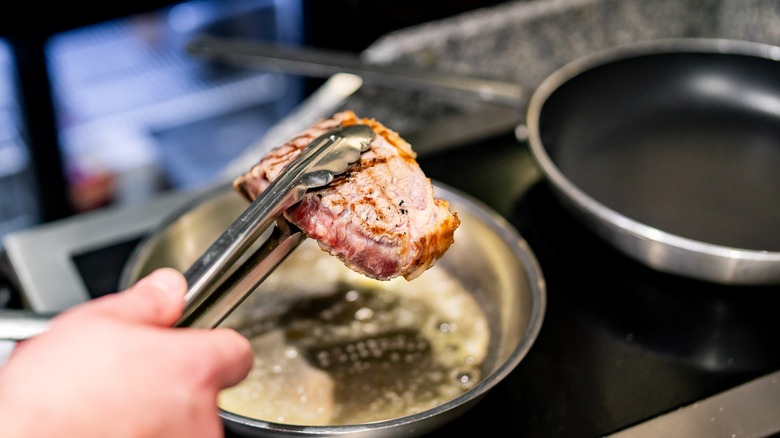 hot steak held with tongs over sizzling pan of butter