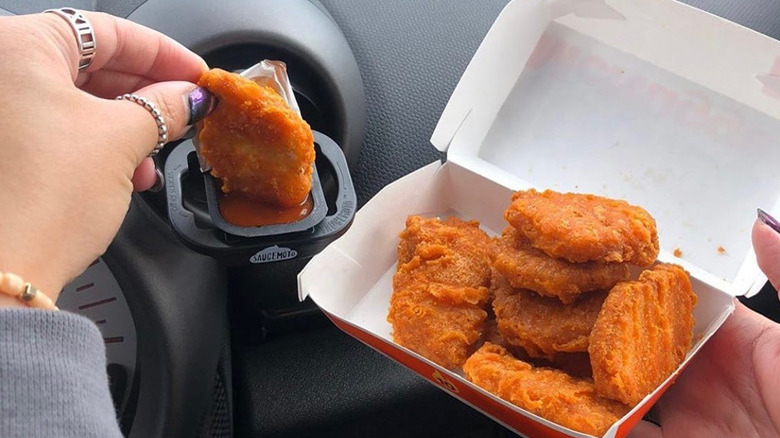 Hand dipping chicken nuggets into sauce in car Saucemoto dip holder