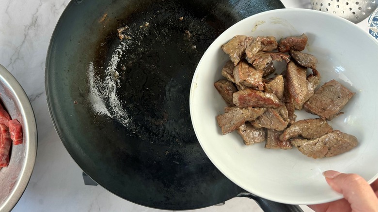 hand holding meat over wok