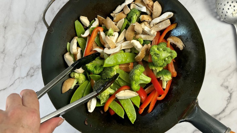 hand stirring vegetables with tongs