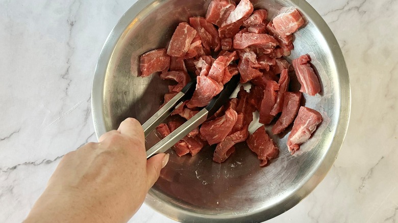 hand stirring meat with tongs