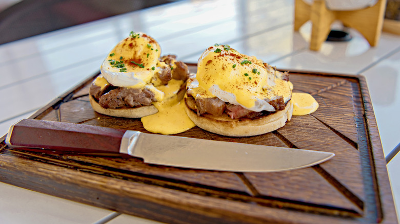 Eggs benedict with steak on a wooden board with a knife