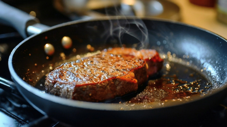 A steak cooking on a stovetop in a black frying pan