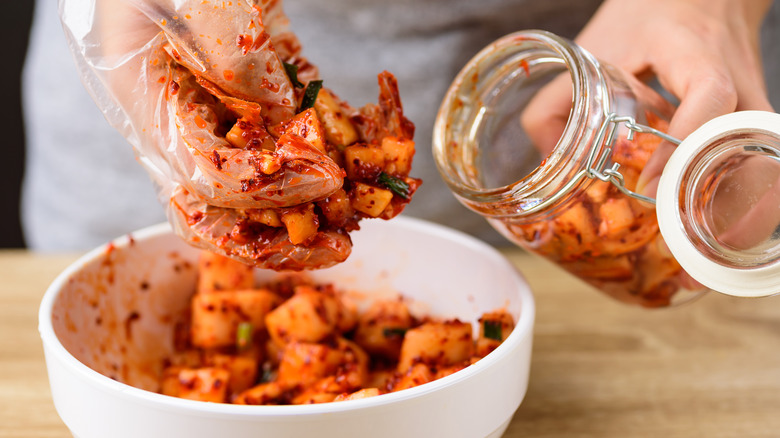 Gloved hands put kimchi in jar