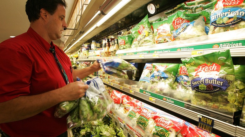 store worker removing bags of greens from shelves