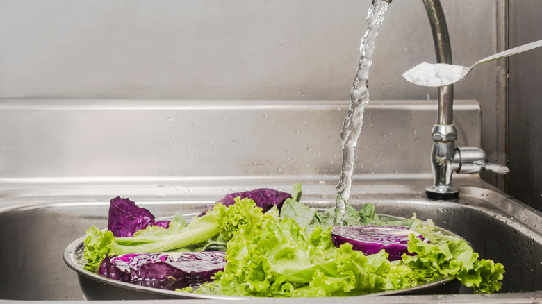 salad greens being washed under a faucet