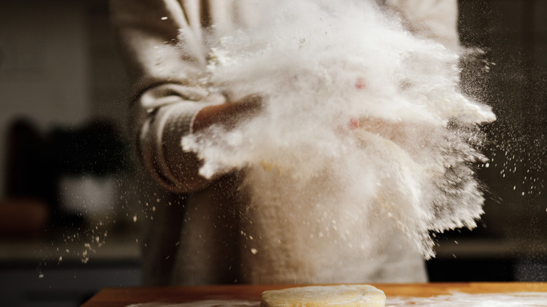 woman throwing handfuls of flour onto counter