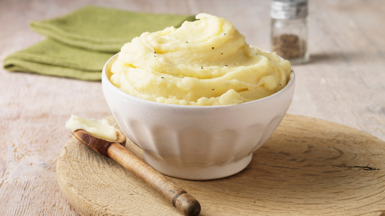 A bowl of mashed potatoes sits alongside a wooden spoon