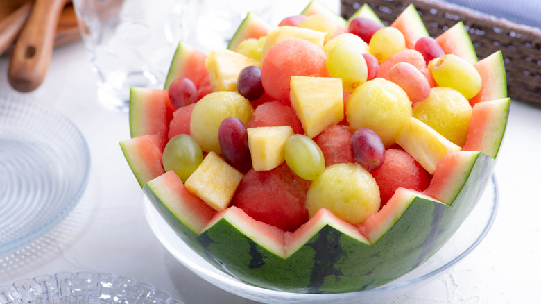 A hollowed-out watermelon with a zigzag pattern cut into the rim holds various cut fruits