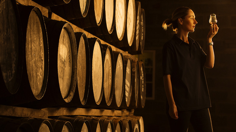 female distiller stands next to whiskey barrels